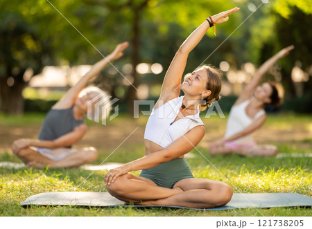 Girl stretching in lotus position group yoga session in park 121738205
