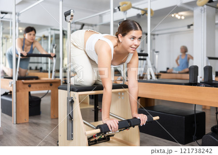 Mature woman practicing pilates stretching exercises on reformer at gym Mature woman practicing pilates stretching exercises on reformer at gym 121738242