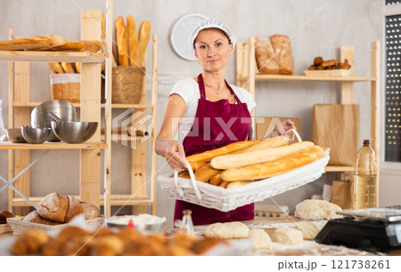 Middle-aged woman holding baguettes in wicker basket Middle-aged woman holding baguettes in wicker basket 121738261