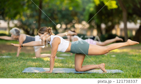 Young girl with group of active people doing stretching exercises during yoga class at city park together Young girl with group of active people doing stretching exercises during yoga class at city park together 121738337