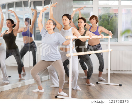Senior woman performing demi plie at barre at fitness session 121738376