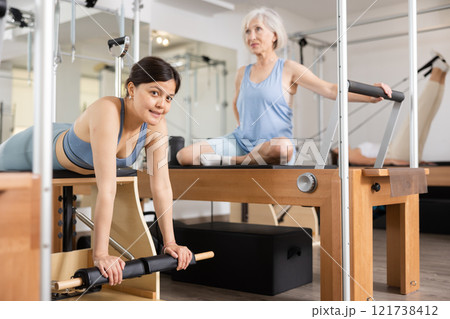 Young positive woman doing Pilates on special equipment in gym Young positive woman doing Pilates on special equipment in gym 121738412