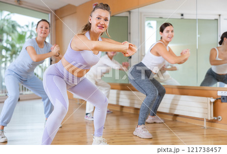 Smiling active women of different ages making squats during dancing training with coach in fitness studio Smiling active women of different ages making squats during dancing training with coach in fitness studio 121738457