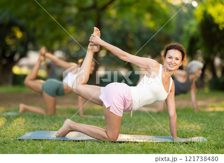 Positive sporty skilled young female teacher demonstrating table pose of yoga in green park at daytime 121738480