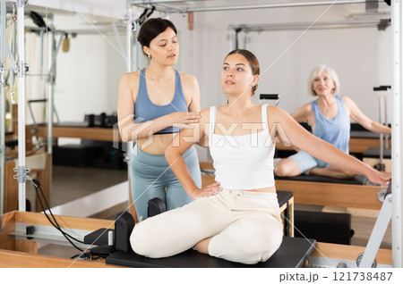 Woman doing pilates in fitness studio with female personal trainer controlling movements 121738487