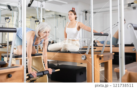 Sporty elderly woman practicing pilates exercises on combo chair 121738511