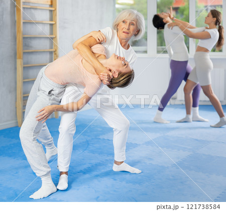 Senior woman applying inverted headlock during mock bout in self-defense training 121738584