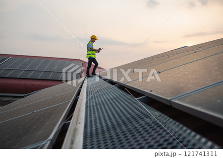man in a yellow vest is standing on a roof, looking at his phone 121741311