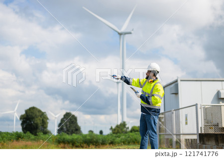 man in a yellow and black safety vest points at a wind turbine 121741776