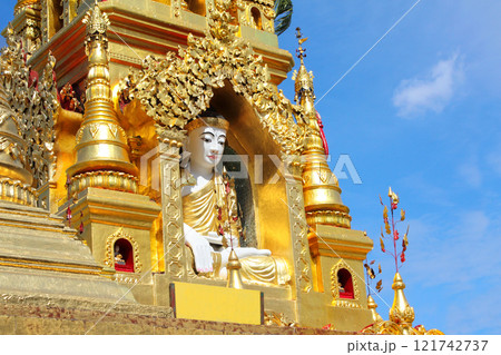 Statue of Buddha in golden ancient buddhist stupa. Stone figure of Buddha near to buddhist temple, Yangon, Myanmar (Burma). On blue sky background Statue of Buddha in golden ancient buddhist stupa. Stone figure of Buddha near to buddhist temple, Yangon, Myanmar (Burma). On blue sky background 121742737