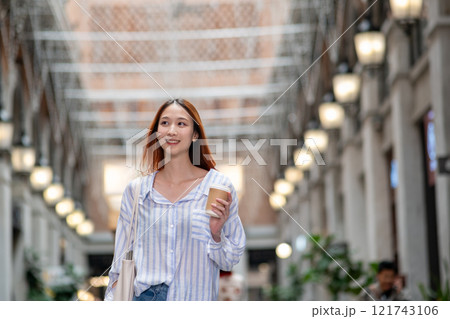Woman is walking down a hallway with a cup of coffee in her hand Woman is walking down a hallway with a cup of coffee in her hand 121743106