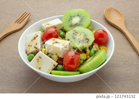 close up view of soft tofu with fruit and vegetables salad topped with sesame sauce in a bowl on wooden table. homemade style healthy food concept. close up view of soft tofu with fruit and vegetables salad topped with sesame sauce in a bowl on wooden table. homemade style healthy food concept. 121743132
