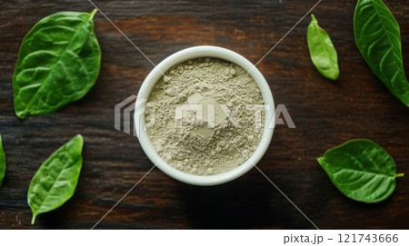 Kratom powder in a white bowl with fresh kratom leaves on a wooden surface, emphasizing natural remedies and herbal wellness. 121743666
