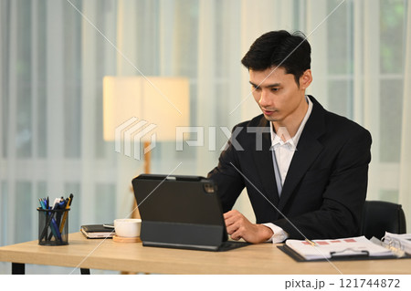 Focused millennial businessman in black suit working on digital tablet in modern office 121744872