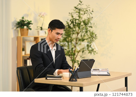Focused millennial businessman in black suit working on digital tablet in modern office 121744873