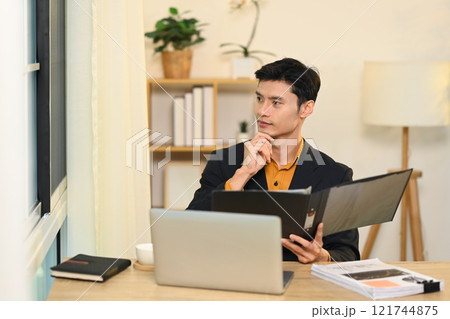 Asian businessman holding folder and looking thoughtfully out of a window 121744875
