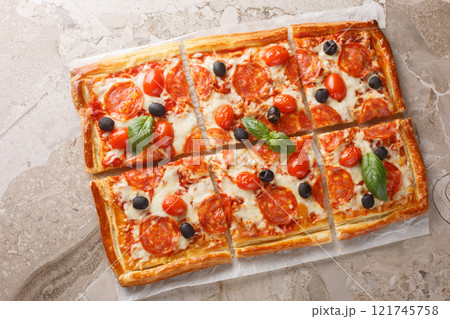 Spicy tart pizza made from puff pastry with pepperoni sausage, olives, cheese and tomato sauce close-up on parchment. horizontal top view 121745758