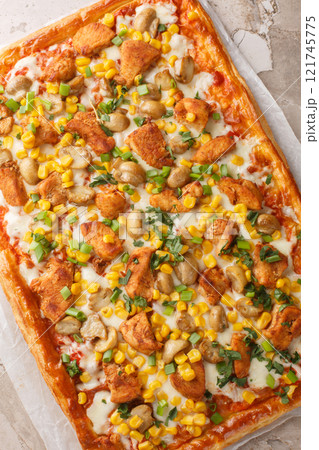 Homemade puff pizza pie with chicken breast, mushrooms, corn, mozzarella cheese and tomato sauce close-up on parchment paper on table. Vertical top view 121745775