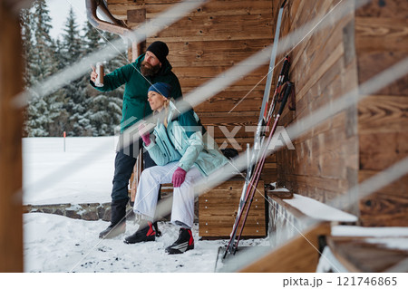 Couple resting after cross country skiing in winter nature, sitting in front cabin. Couple resting after cross country skiing in winter nature, sitting in front cabin. 121746865