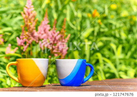 Tea time. Coffee break. Blue yellow cups on wooden in blooming garden Tea time. Coffee break. Blue yellow cups on wooden in blooming garden 121747676