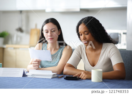 Serious interracial roommates calculating expenses in the kitchen Serious interracial roommates calculating expenses in the kitchen 121748353