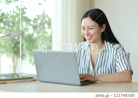 Happy asian woman using laptop in a room Happy asian woman using laptop in a room 121748380