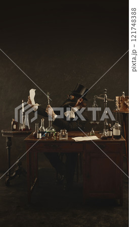 Plague doctor dressed in suit sits at table in vintage laboratory and checks prescription with magnifying glass against dark mystery background. Plague doctor dressed in suit sits at table in vintage laboratory and checks prescription with magnifying glass against dark mystery background. 121748388