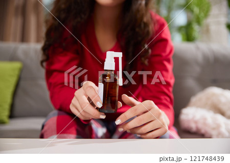 Cropped photo of woman holds brown glass spray bottle with white nozzle while sitting on sofa in living room. Cropped photo of woman holds brown glass spray bottle with white nozzle while sitting on sofa in living room. 121748439