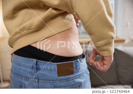 Man lifts his beige sweater to expose his lower back, preparing for medical injection. Treatment at home. Man lifts his beige sweater to expose his lower back, preparing for medical injection. Treatment at home. 121748464