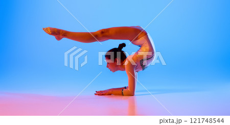 Athlete maintains balanced pose as part of rigorous training routine in pink neon light against gradient blue background. 121748544