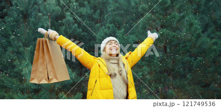 Happy smiling young woman with shopping bag in winter against Christmas tree, holiday shopping Happy smiling young woman with shopping bag in winter against Christmas tree, holiday shopping 121749536