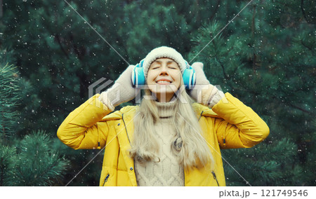 Happy young woman enjoy listening to music with headphones in winter forest against Christmas tree Happy young woman enjoy listening to music with headphones in winter forest against Christmas tree 121749546