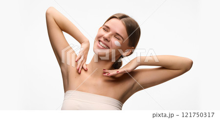 Happy, young woman smiling cheerfully with cream on cheeks, radiating elegance and skincare routines against white studio background. Concept of natural beauty. Happy, young woman smiling cheerfully with cream on cheeks, radiating elegance and skincare routines against white studio background. Concept of natural beauty. 121750317