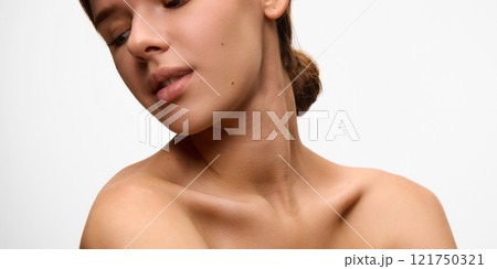 Beautiful young woman tilts her head gracefully, showcasing her flawless neck and collarbone against white studio background. Concept of natural beauty. 121750321