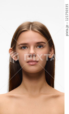 Portrait of confident, beautiful young woman posing against white studio background. Female model with well-kept, smooth, flowless skin. Concept of natural beauty. 121750335