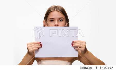 Woman confidently holding blank paper to insert your text horizontally in front of her against white studio background. Concept of natural beauty. Woman confidently holding blank paper to insert your text horizontally in front of her against white studio background. Concept of natural beauty. 121750352