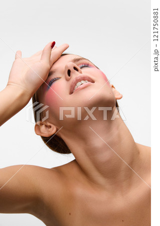 Young woman, with bright make up, tilting head back and put hand on face, against white studio background. Concept of unique beauty. 121750881