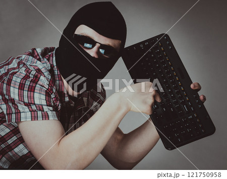 Man wearing balaclava holding keyboard 121750958