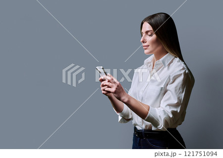 Profile view, young beautiful woman using mobile phone on grey background Profile view, young beautiful woman using mobile phone on grey background 121751094