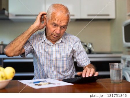 Elderly male sits at the table and looks through bills and checks Elderly male sits at the table and looks through bills and checks 121751846