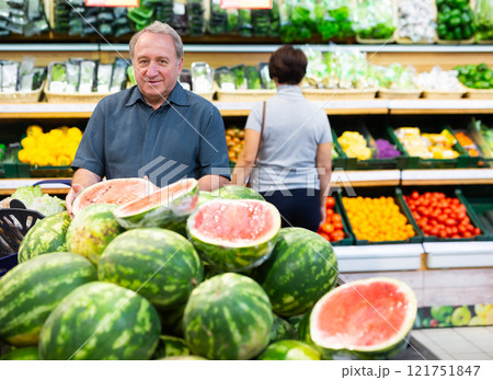 Satisfied man chooses ripe sweet watermelon on grocery store window Satisfied man chooses ripe sweet watermelon on grocery store window 121751847