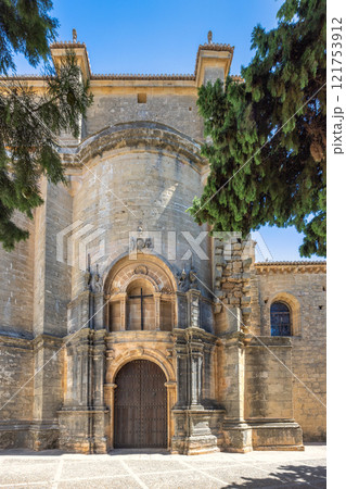 Ronda town in Spain. Ancient stone church entrance under a clear blue sky. Intricate details and aged wood door. 121753912