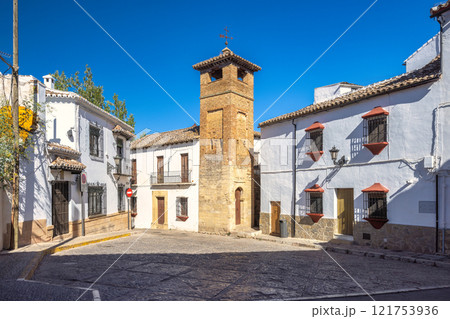 Ronda town in Spain. Historic town square with a distinctive stone tower and whitewashed buildings under a vibrant blue sky. 121753936