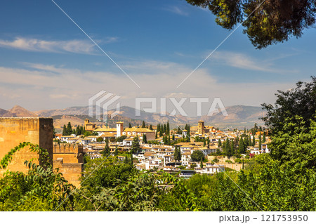 Granada town in Spain. Panoramic view of a charming town nestled in a valley, surrounded by mountains under a clear blue sky.  A picturesque scene of traditional architecture. 121753950