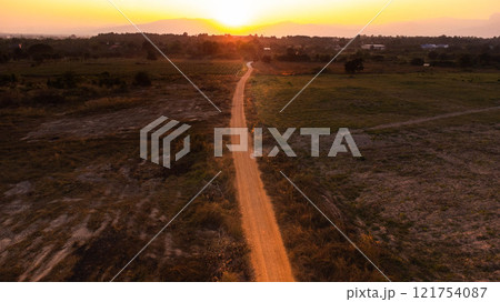 Country road through pasture. Sunrise over a dirt road. Dusty rural road landscape and a beautiful sunset sky use for natural background. 121754087