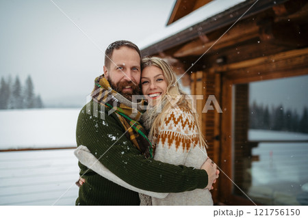 Couple hugging in front of a cabin during snowfall. Romantic weekend trip for mature couple. Couple hugging in front of a cabin during snowfall. Romantic weekend trip for mature couple. 121756150