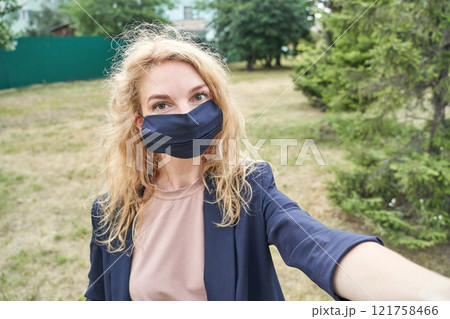 Caucasian young female in mask taking selfie in outdoor park setting with trees 121758466