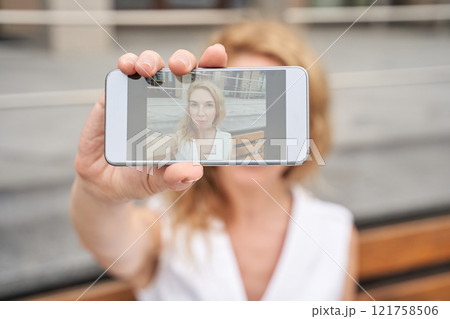 Caucasian female adult taking self-portrait with smartphone, blurred background Caucasian female adult taking self-portrait with smartphone, blurred background 121758506