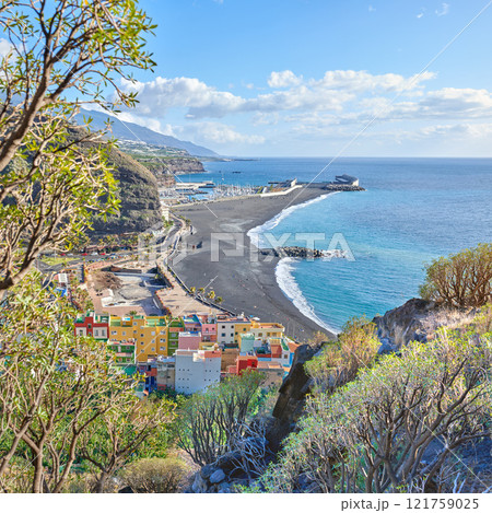 An ocean coast with black beach sand on Puerto de Tazacorte beach from above. Colorful town houses or holiday resort accommodation near the seaside in a beautiful tourism destination, La Palma, Spain An ocean coast with black beach sand on Puerto de Tazacorte beach from above. Colorful town houses or holiday resort accommodation near the seaside in a beautiful tourism destination, La Palma, Spain 121759025