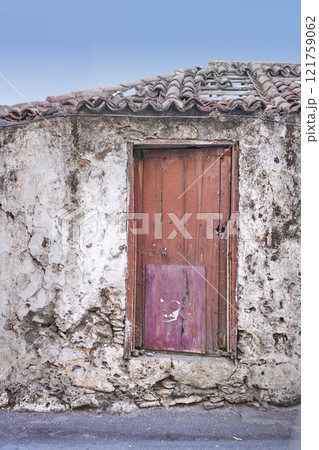 Old abandoned house or home with a weathered stone wall and red wooden door. Vintage and aged residential building built in a traditional architectural style or design with a blue sky background Old abandoned house or home with a weathered stone wall and red wooden door. Vintage and aged residential building built in a traditional architectural style or design with a blue sky background 121759062